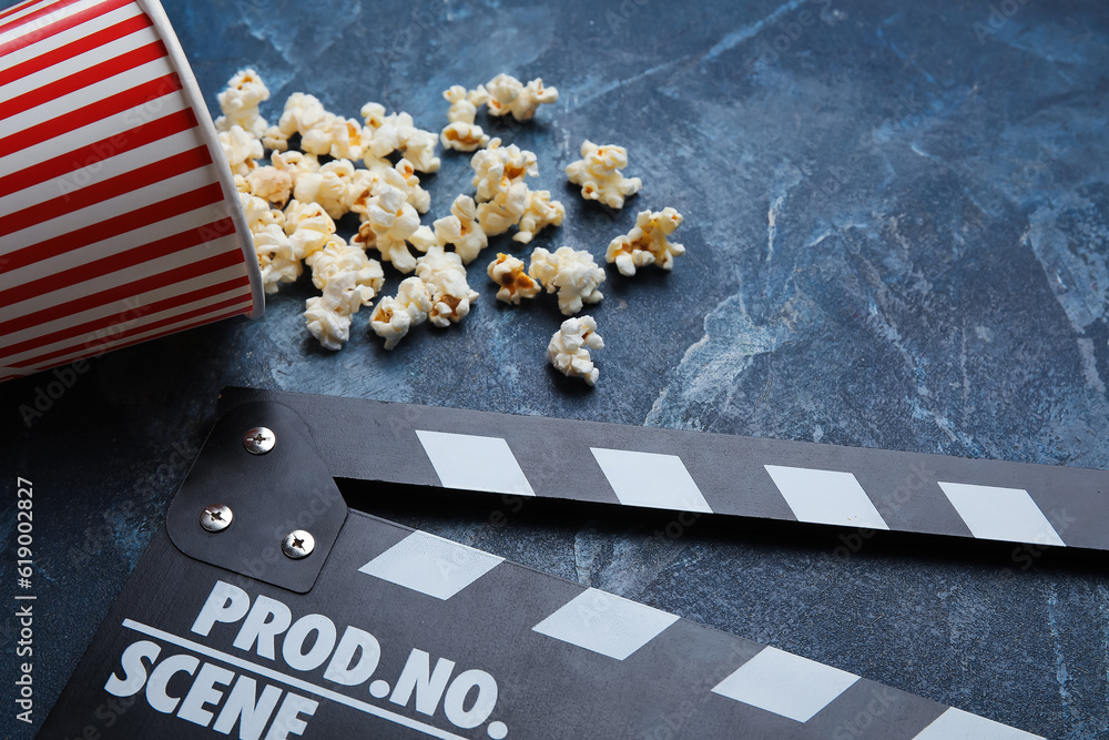 Bucket with tasty popcorn and clapperboard on blue background