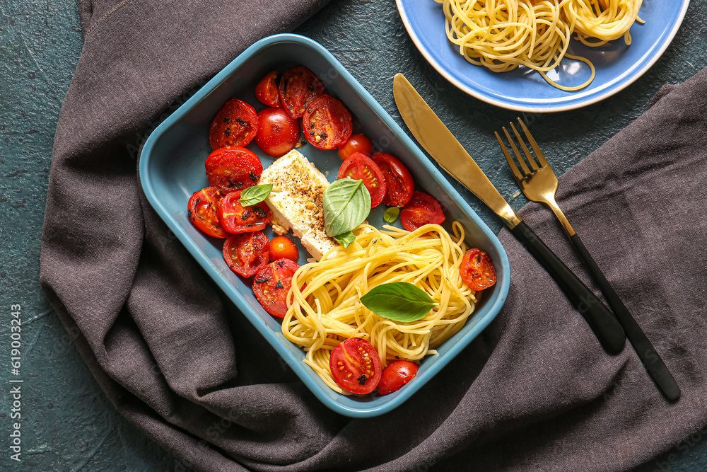 Baking dish of tasty pasta with tomatoes and feta cheese on blue background