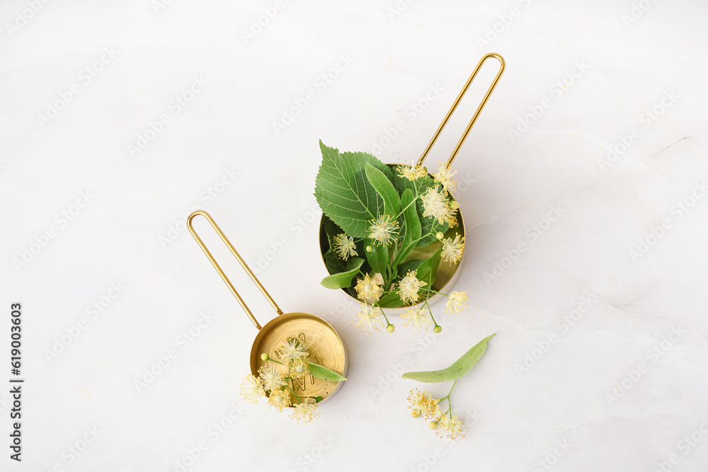 Golden saucepans with aromatic linden flowers on light background