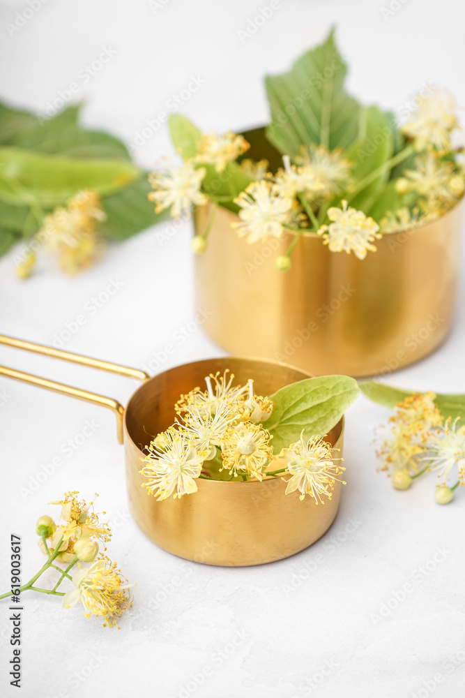 Golden saucepans with aromatic linden flowers on light background, closeup