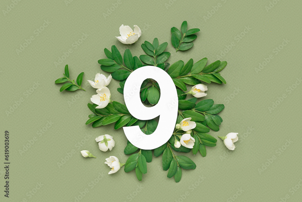 Leaves and white flowers with paper number nine on green background