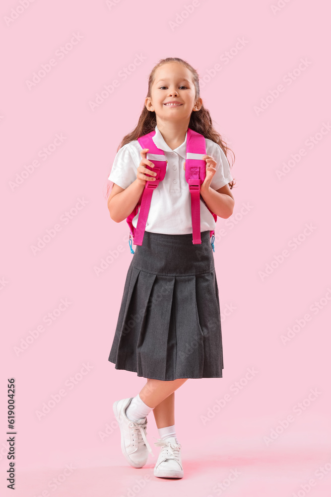 Little schoolgirl with backpack on pink background