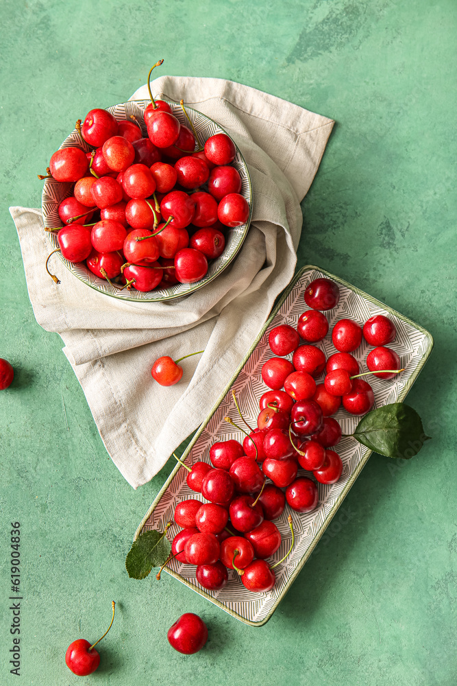 Plate and bowl with sweet cherries on green background