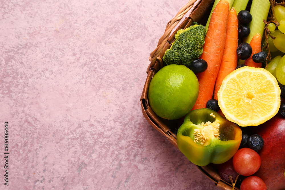 Wicker basket with different fresh fruits and vegetables on pink background, closeup