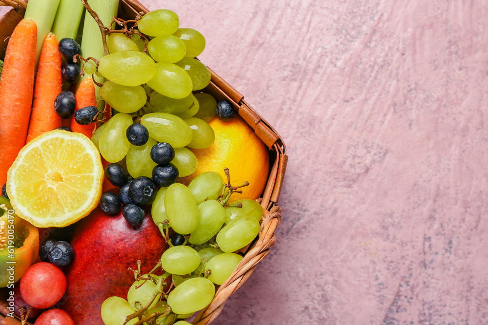 Wicker basket with different fresh fruits and vegetables on pink background, closeup