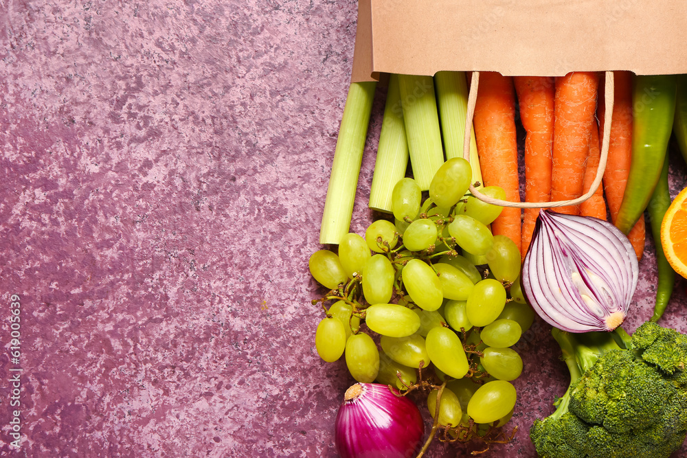 Paper bag with different fresh fruits and vegetables on purple background