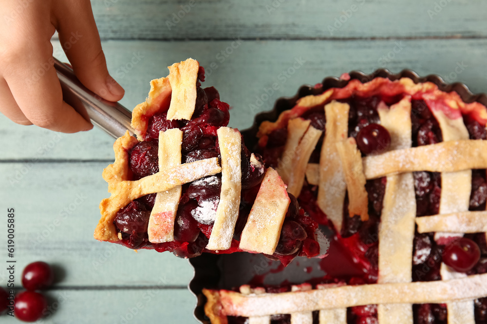 Woman taking piece of tasty cherry pie on blue wooden table