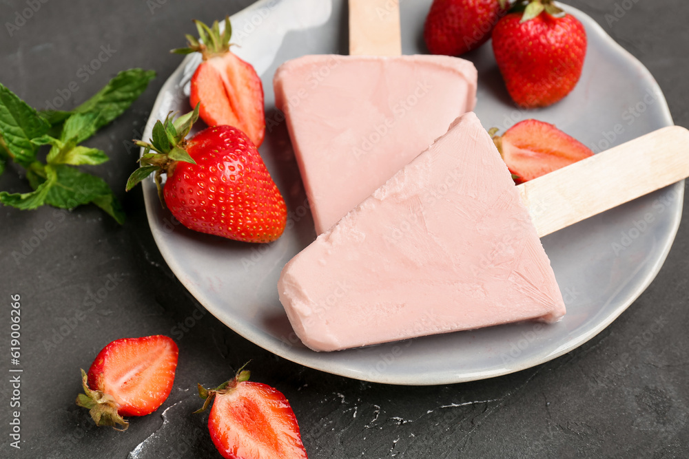 Plate with sweet strawberry ice-cream popsicles on black background