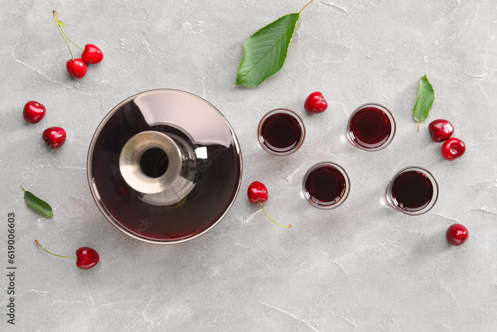 Shots and bottle with sweet cherry liqueur on grey background