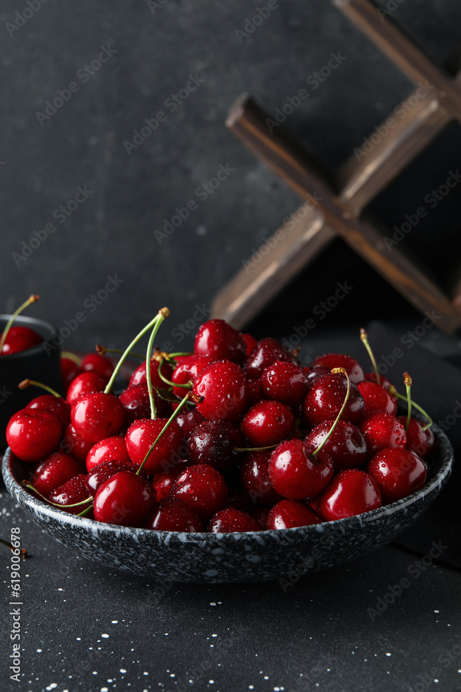 Bowl with sweet cherries on black background