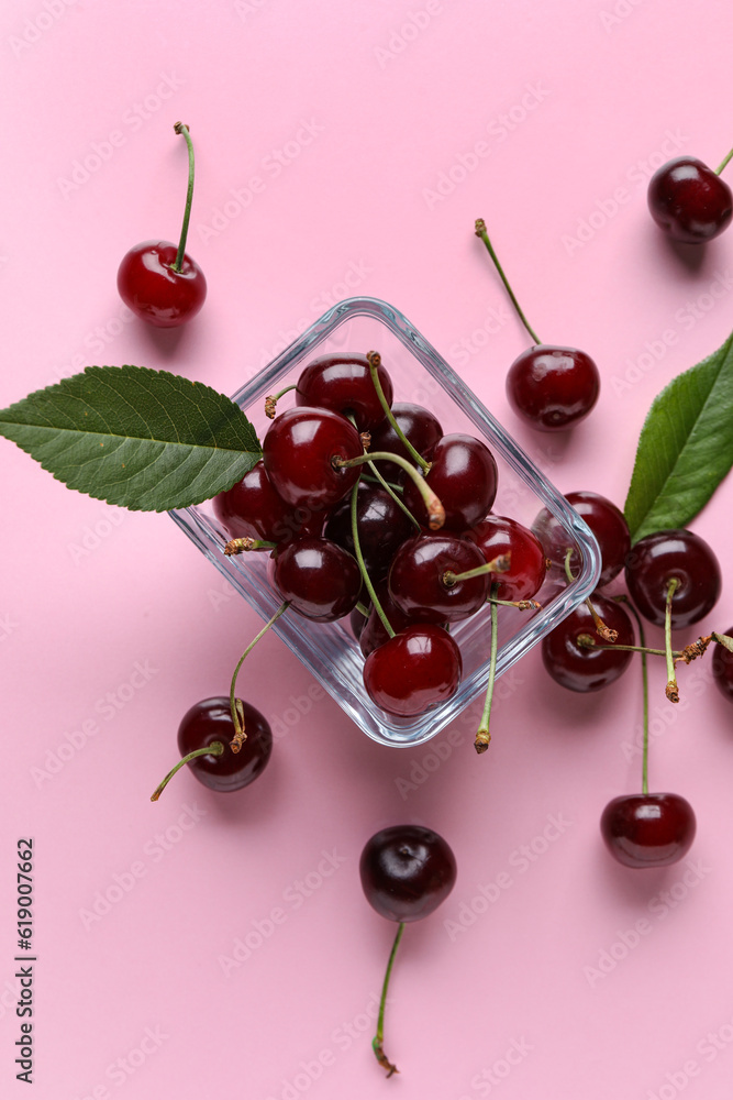 Glass bowl with sweet cherries and leaves on pink background