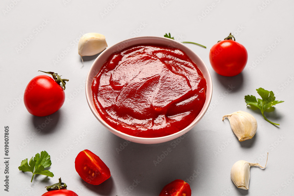 Bowl with tomato paste and fresh vegetables on grey background