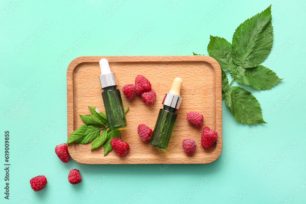 Wooden board with bottles of cosmetic raspberry oil on blue background