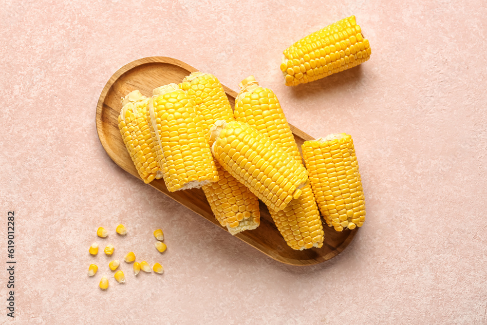 Wooden board with fresh corn cobs on pink background