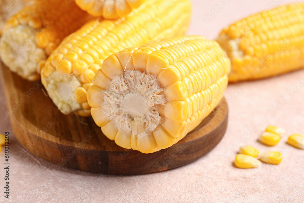 Wooden board with fresh corn cobs on pink background