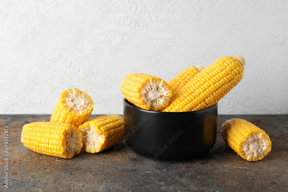 Bowl with fresh corn cobs on dark table