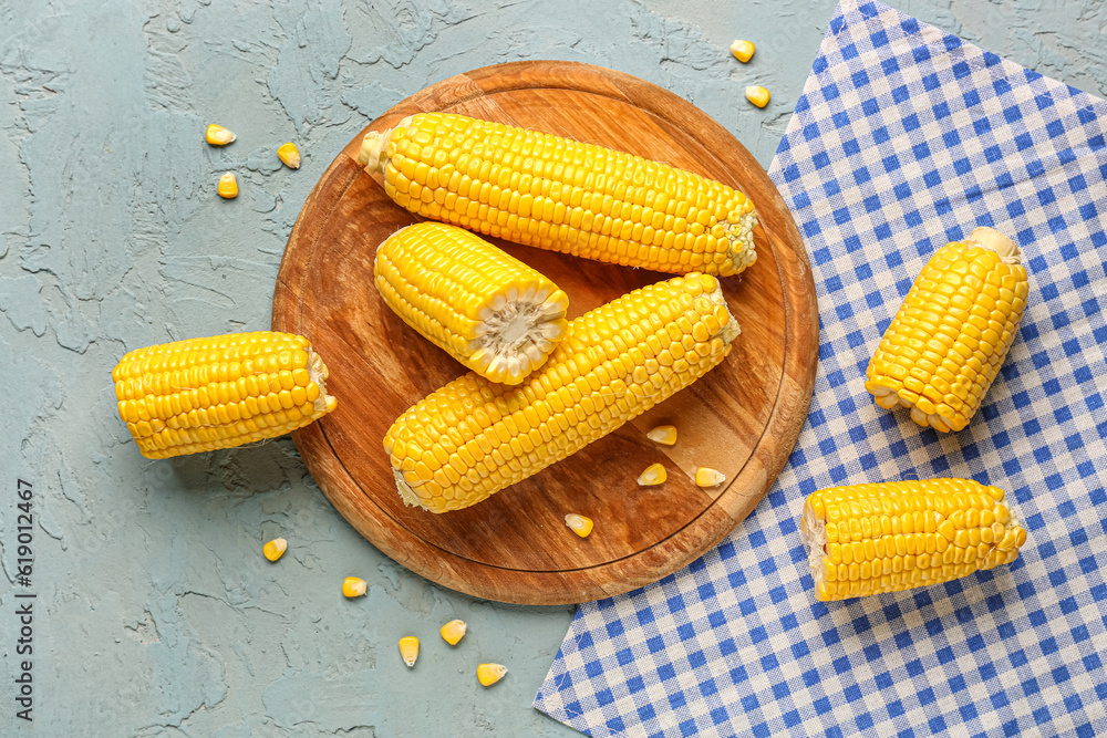 Wooden board with fresh corn cobs and seeds on blue background