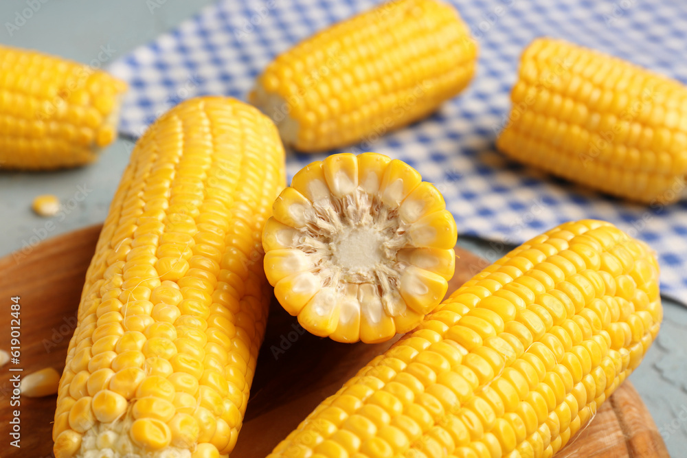 Wooden board with fresh corn cobs on blue background