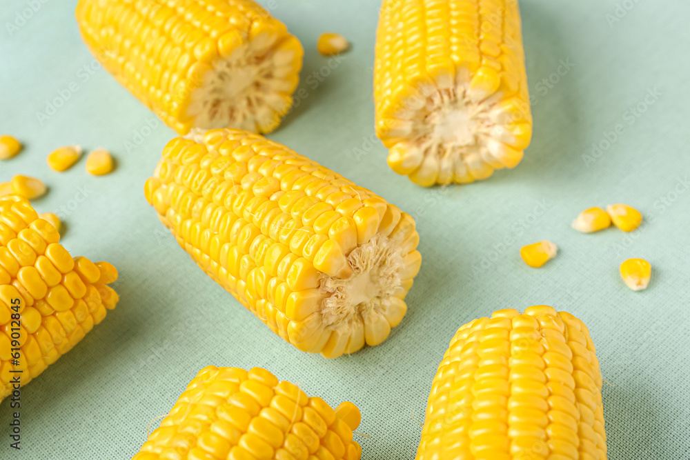 Cut fresh corn cobs and seeds on green background, closeup