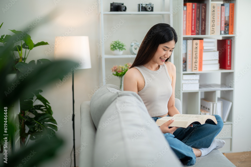 Asian beautiful woman sitting happily reading a book on the sofa in the living room.