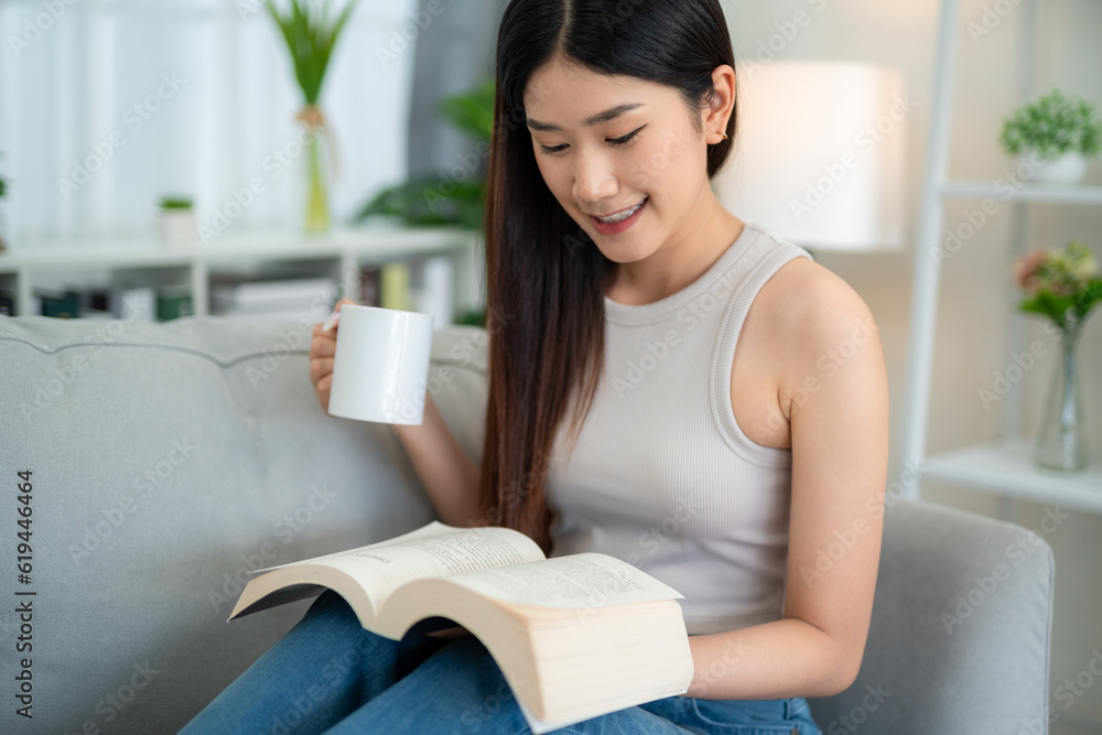 Close up of Asian young woman reading a book with coffee on the sofa in the living room in the morni