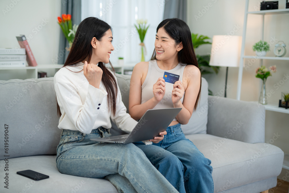 Two young Asian women successfully use credit cards to make purchases. Shopping online with a laptop