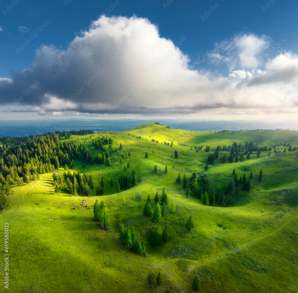 Aerial view of green alpine meadows on the hills at sunset in summer. Top drone view of mountain val