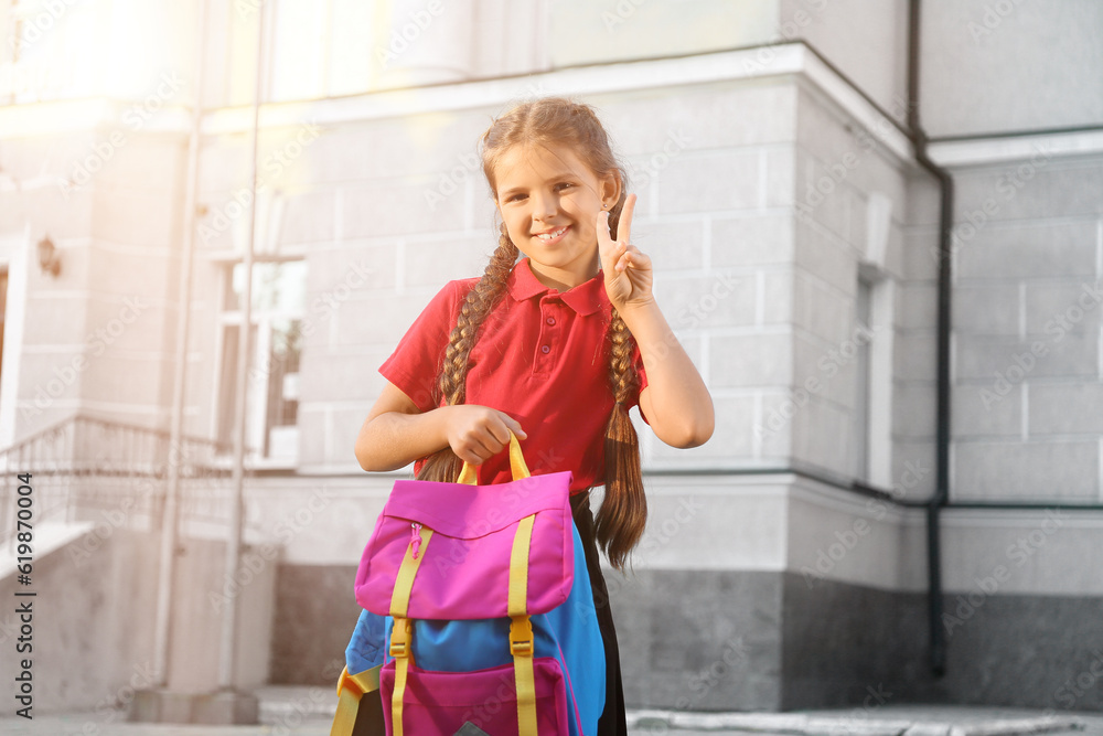 Portrait of cute little schoolgirl showing victory gesture outdoors