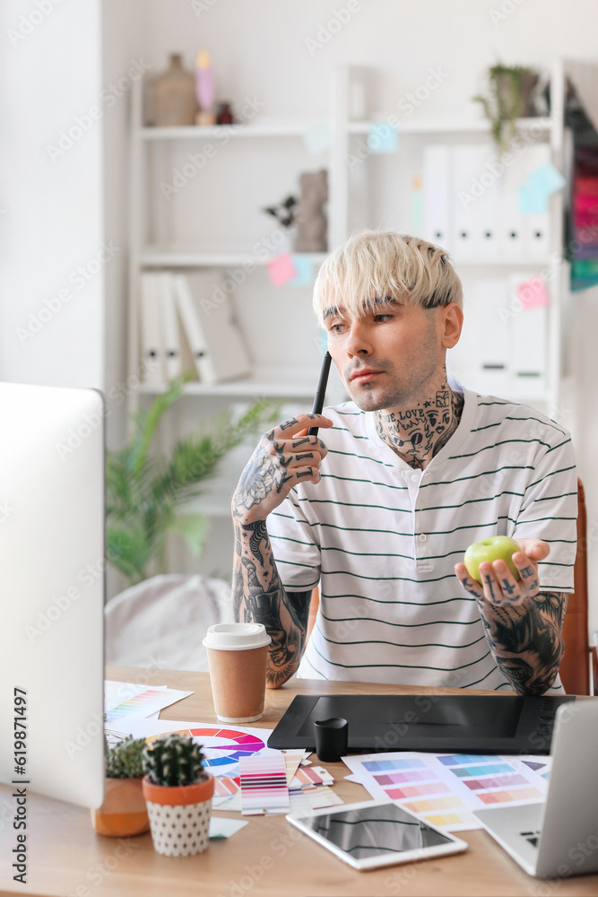 Tattooed graphic designer with apple working at table in office