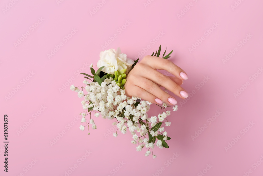 Female hand with white flowers visible through hole in pink paper