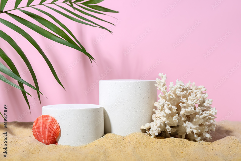 Decorative plaster podiums, seashell and coral in sand on pink background