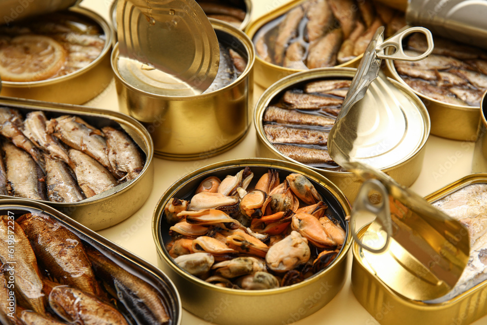 Many opened tin cans with different fish on beige background