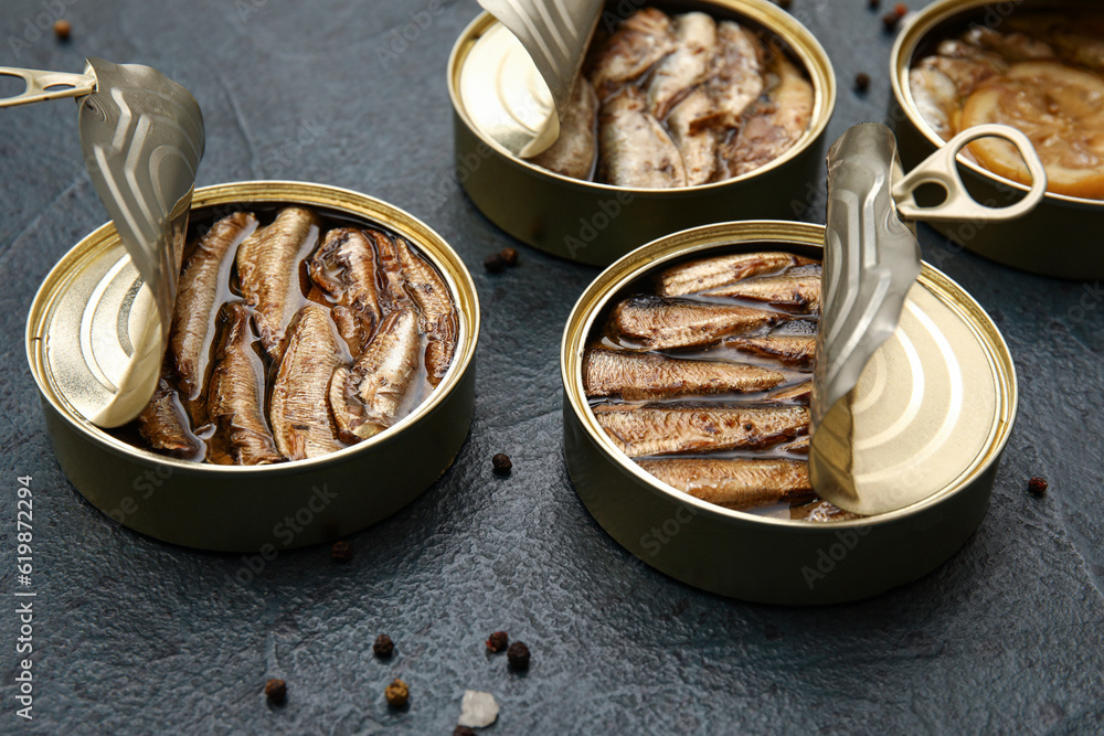 Opened tin cans with sprats in oil on black table