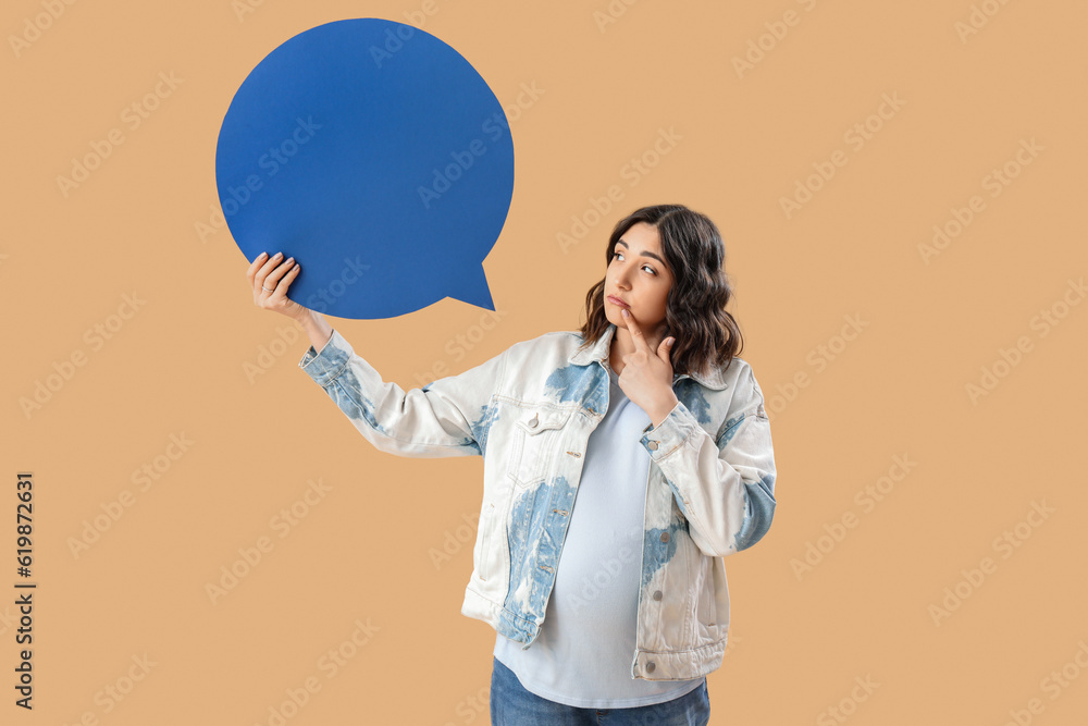 Thoughtful young pregnant woman with blank speech bubble on beige background