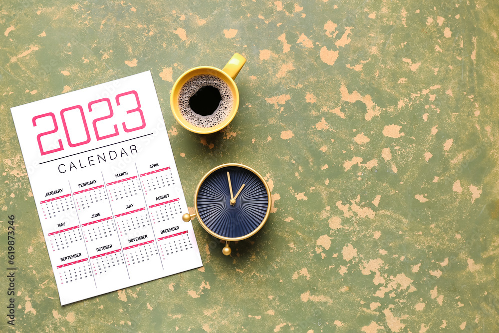 Calendar, alarm clock and cup of coffee on green table