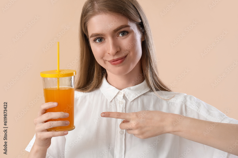 Young woman pointing at glass of carrot juice on beige background, closeup