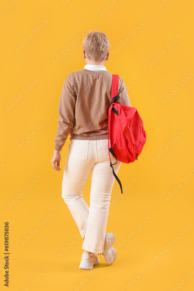 Female student with backpack on yellow background, back view