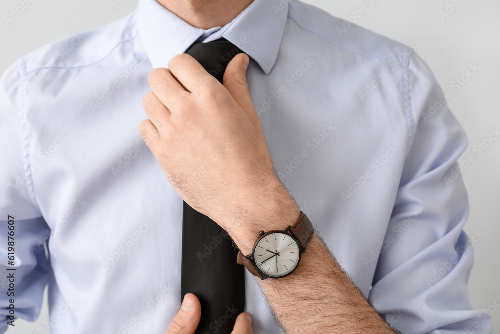 Young businessman fixing necktie on light background, closeup