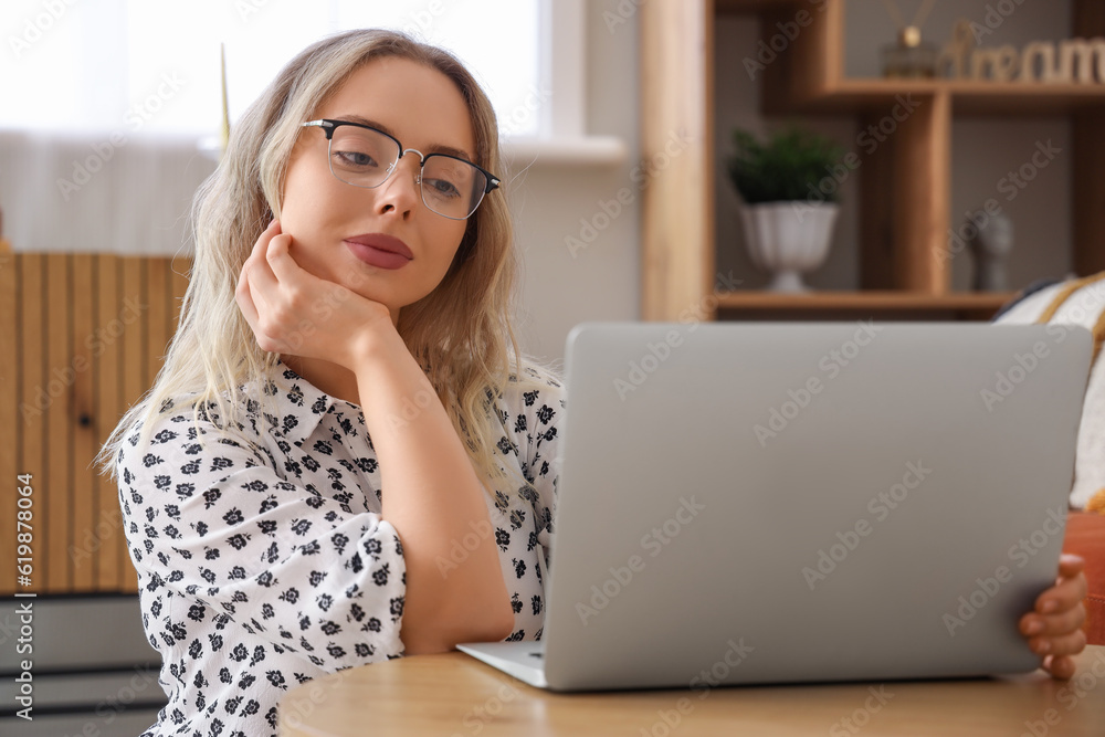 Young woman in stylish eyeglasses using laptop at home