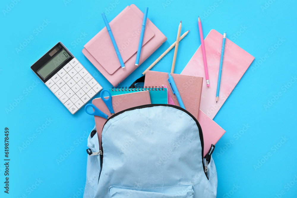 Color school backpack with calculator, notebooks and pencils on blue background