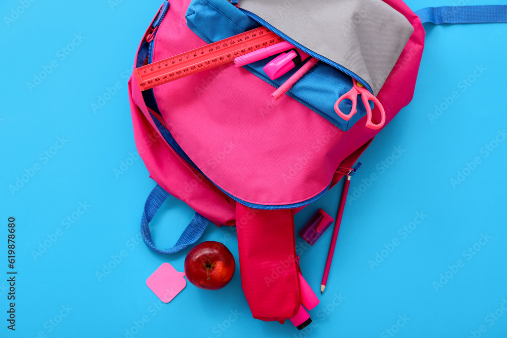 Pink school backpack with apple, ruler and markers on blue background