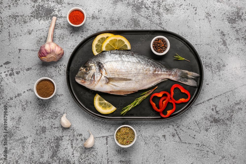 Tray of raw dorado fish with lemon and spices on light background