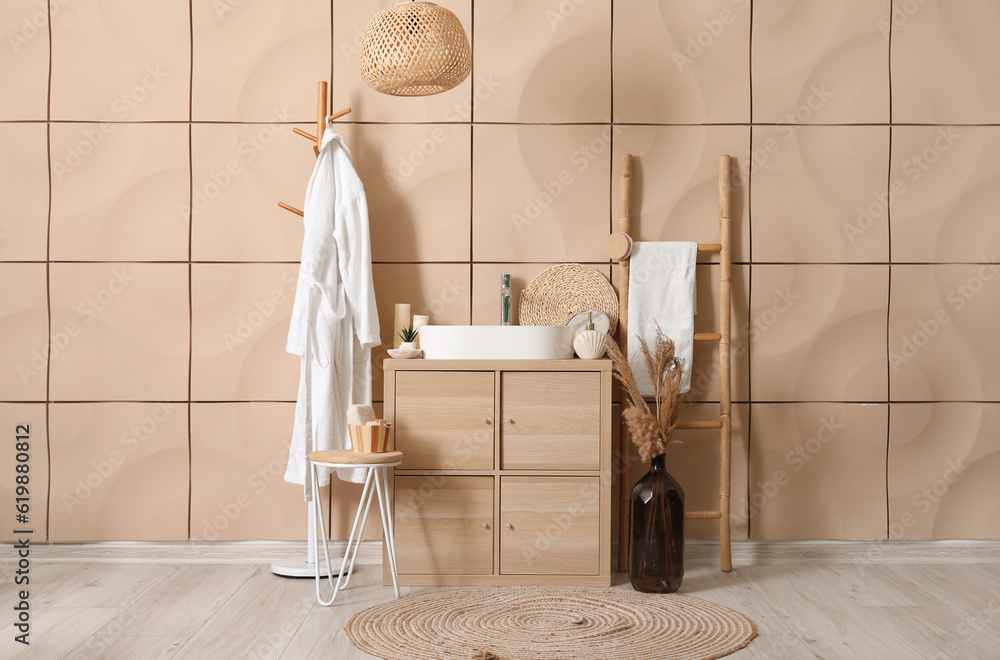 Interior of bathroom with bathrobe, sink bowl and bath accessories on wooden cabinet