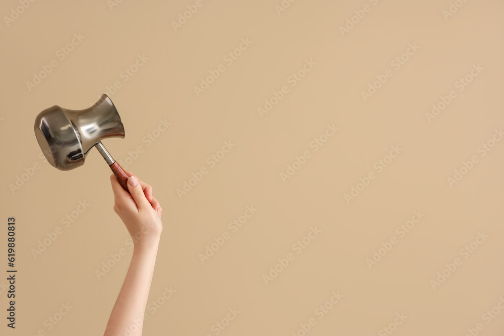 Female hand holding jezve on brown background