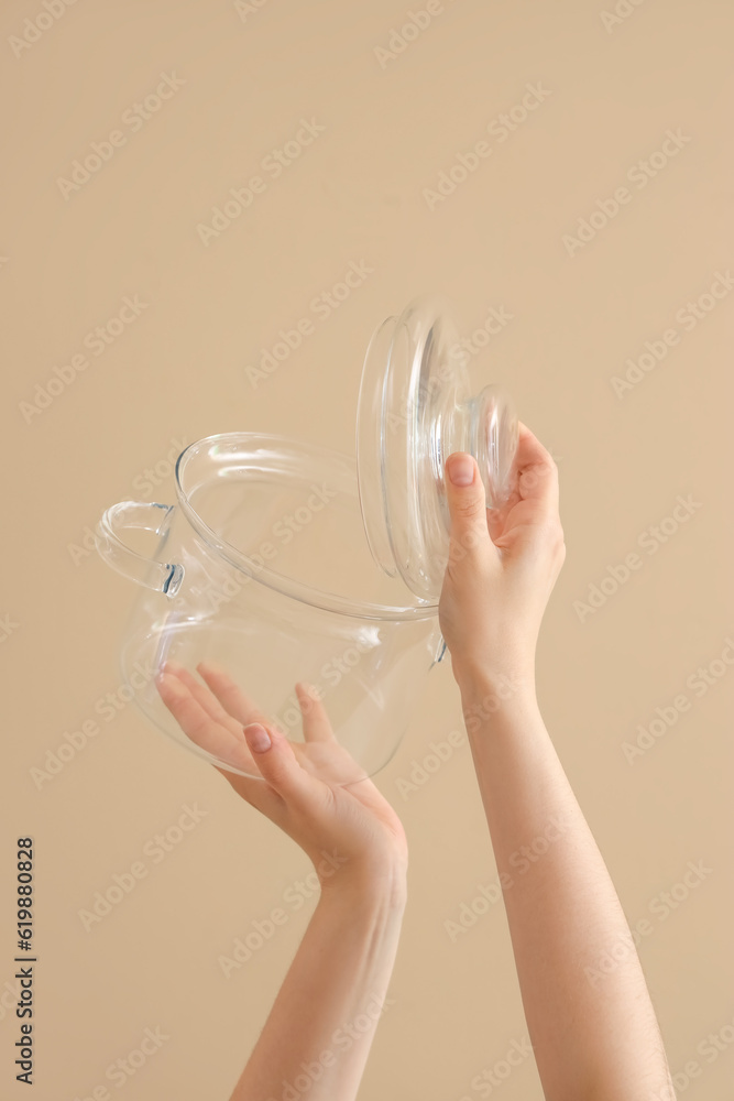 Female hands holding cooking pot and lid on brown background