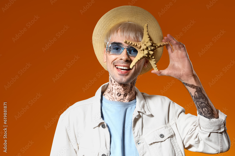 Young tattooed man in stylish sunglasses with starfish on color background