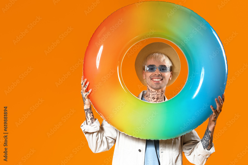 Young tattooed man in stylish sunglasses with inflatable ring on color background