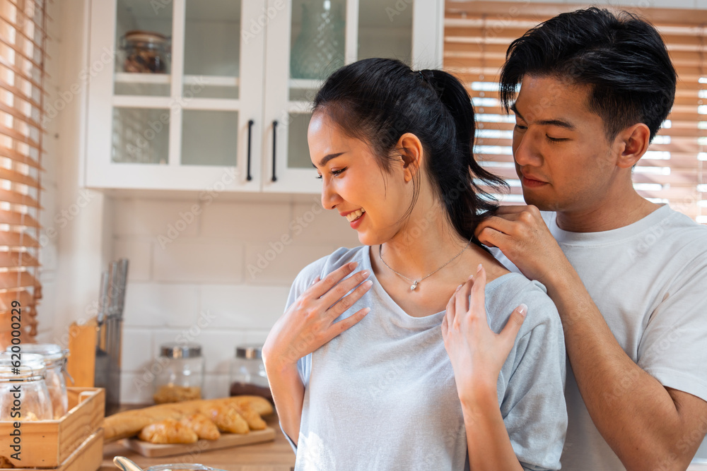 Asian romantic man making surprise girlfriend with necklace in kitchen. 