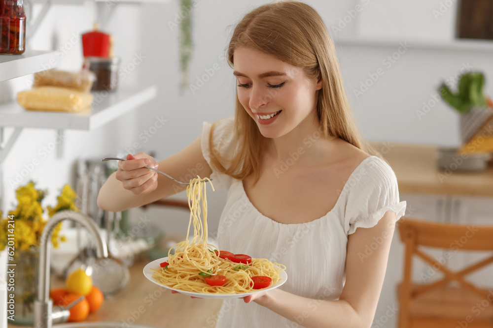 Young woman eating tasty pasta in kitchen