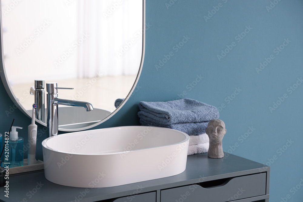 White sink with bath accessories on table near color wall, closeup